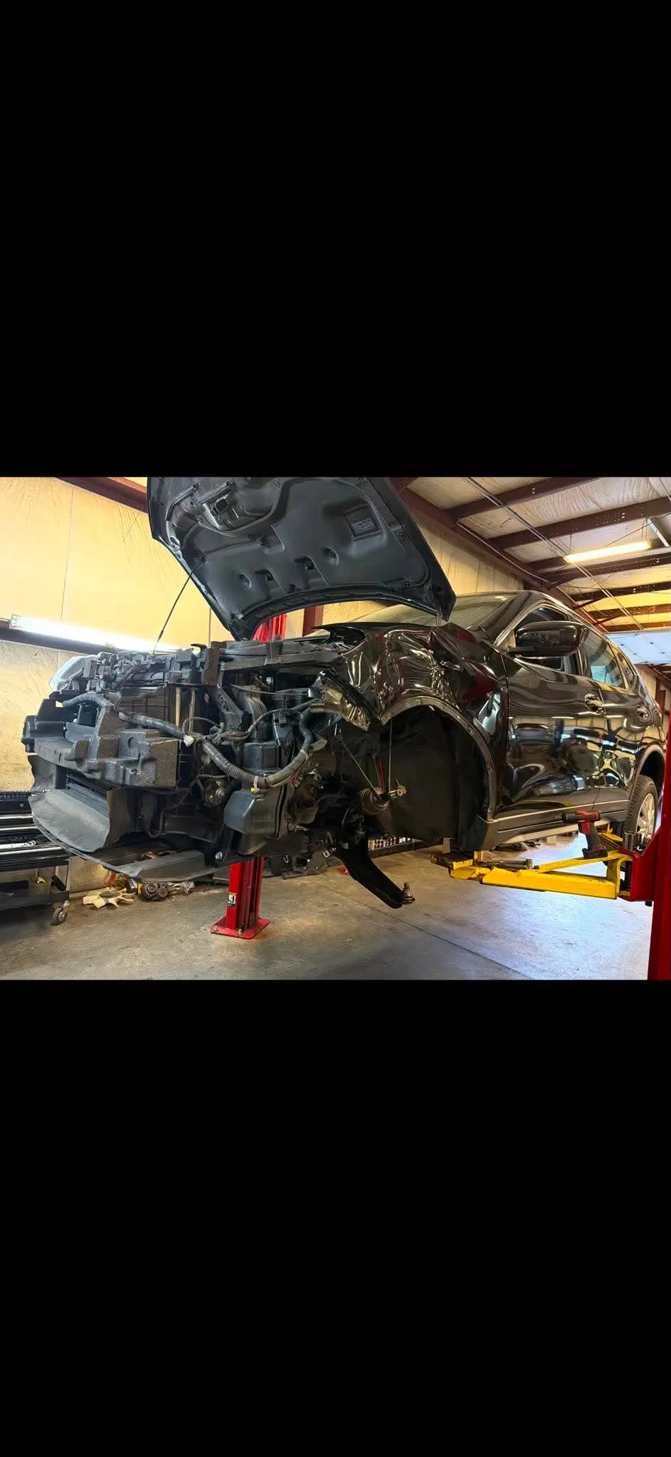 Collision Repair Wide — Wide shot of a black SUV undergoing front-end collision repair on a yellow two-post lift.