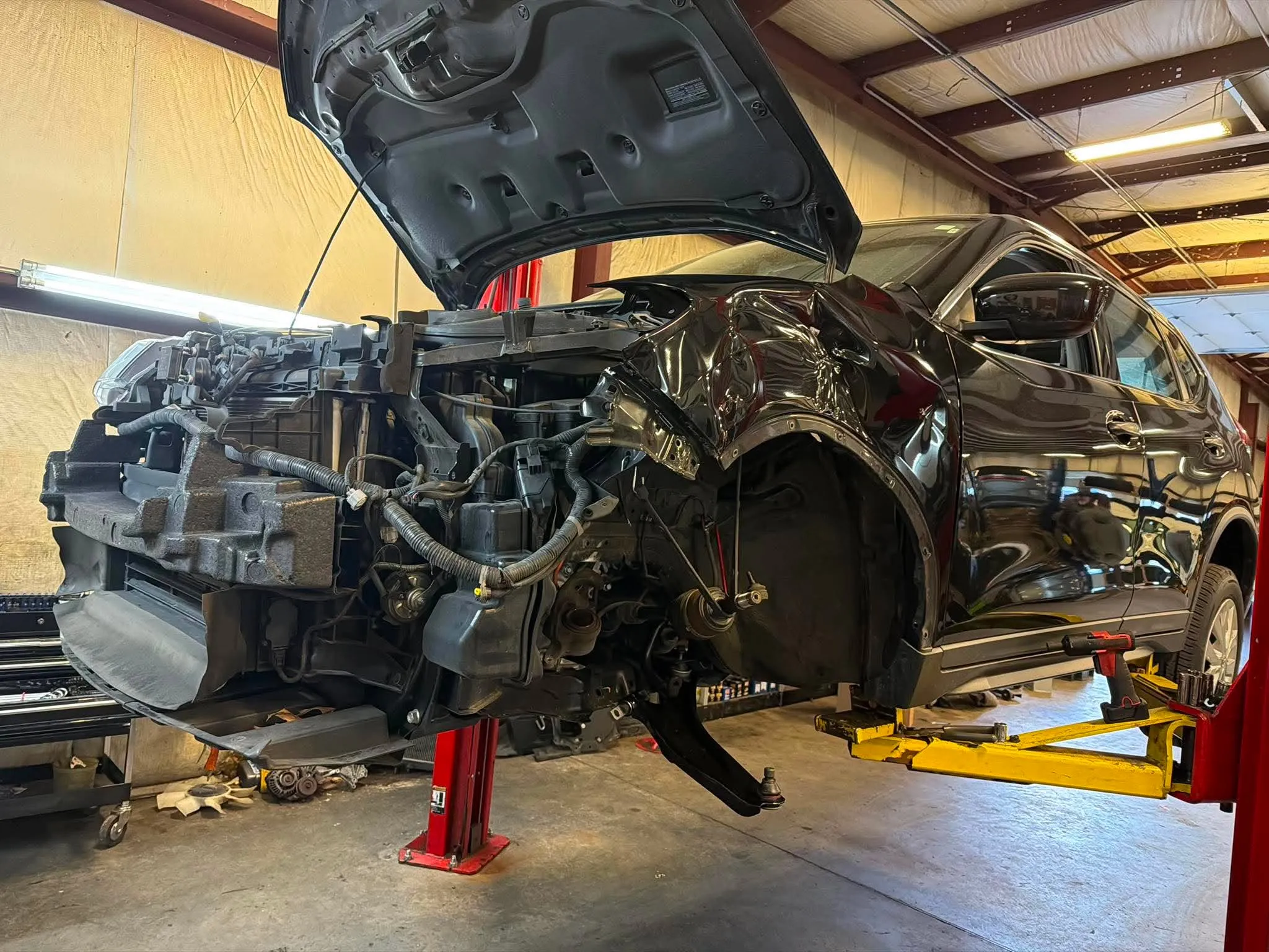 Collision Repair — Black SUV on a lift with its front bumper cover removed, exposing the front crash bar and cooling system.