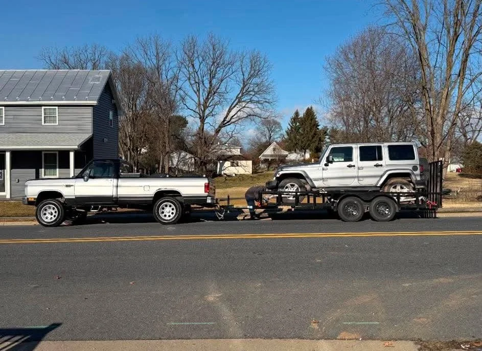 Dodge Towing Jeep — Silver first-generation Dodge Ram pickup truck towing a trailer with a silver Jeep Wrangler loaded on it.
