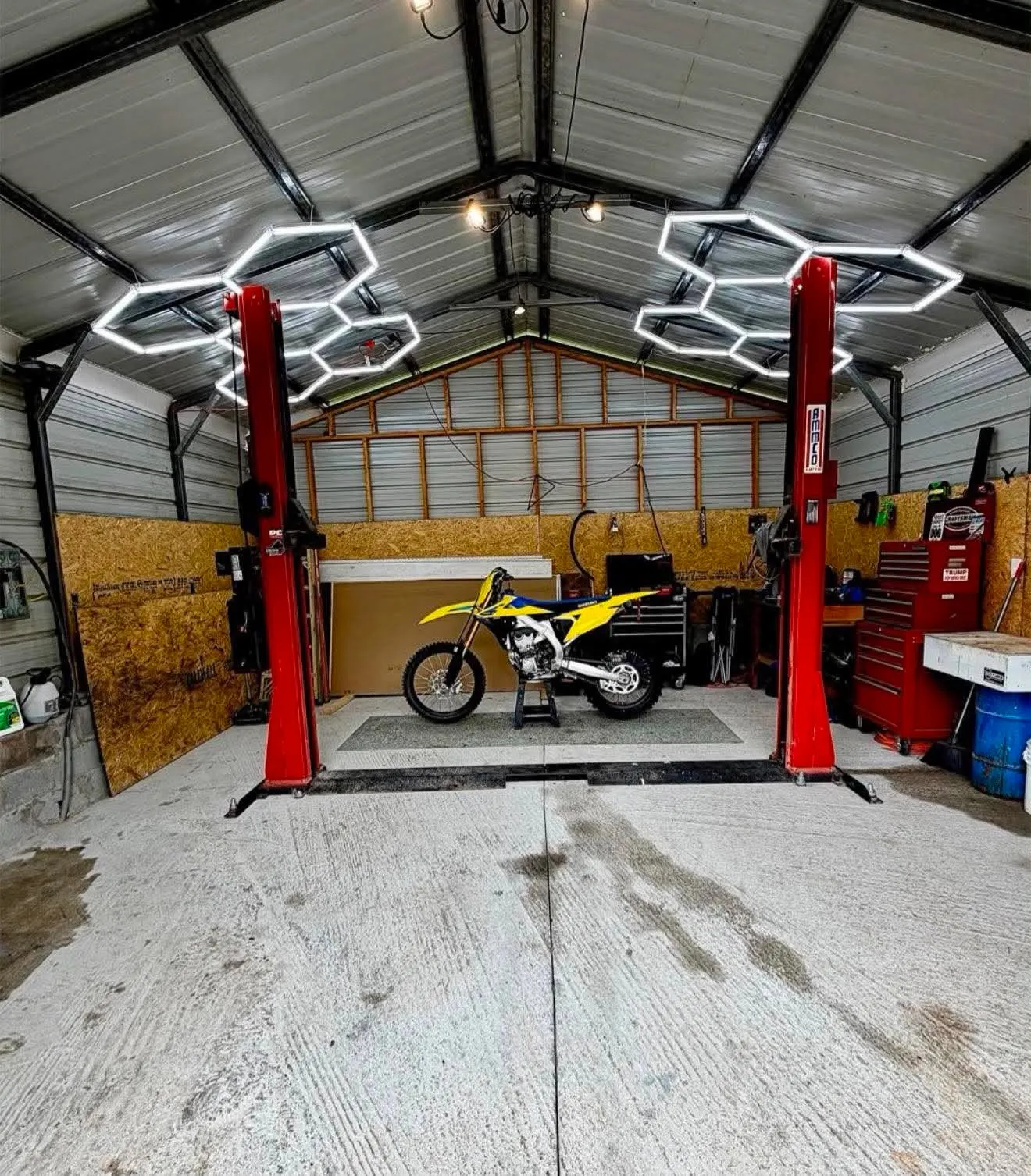 Garage Dirtbike — Yellow Suzuki dirtbike inside a modern garage with hexagon lights and red two-post lifts.