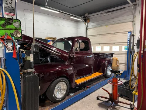 Maroon Classic Truck — Dark maroon classic vintage pickup truck elevated on a drive-on lift inside the garage with the hood open.