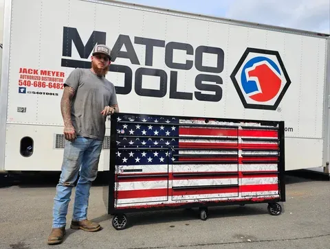 J&H Precision Auto Repair owner standing next to a Matco Tools toolbox adorned with an American flag graphic, holding a wrench inside the Broadway VA workshop.