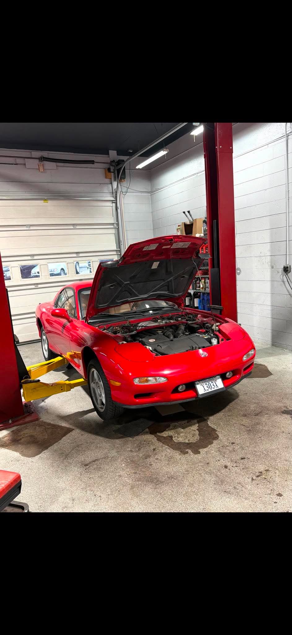 Mazda RX-7 — Bright red Mazda RX-7 (FD generation) sports car on a two-post lift with its hood open for service.